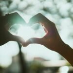 Two hands making a heart shape with the sun shining
